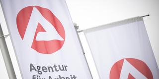 Eine Fahne mit dem Logo der Agentur für Arbeit weht im Wind. (Foto: picture alliance/dpa | Philip Dulian)
