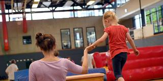 Ein Kind wird beim Kinderturnen von einer Erwachsenen auf dem Schwebebalken geführt (Foto: picture alliance / Britta Pedersen / dpa-Zentralbild / dpa)