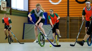 Mehrer Personen fahren in einer Sporthalle auf Einrädern und halten dabei Hockeyschläger in den Händen. (Foto: IMAGO)