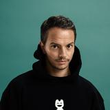 DJ Alle Farben steht in einem schwarzen Hoodie vor einer dunkelgrünen Wand. (Foto: Pressefoto/Alle Farben)