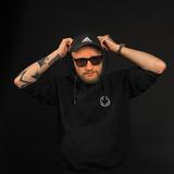 Ein Mann steht mit Sonnenbrille und schwarzer Kappe vor einem schwarzen Hintergrund. Er trägt einen schwarzen Hoodie und hat die Kapuze aufgesetzt. (Foto: Pressefoto)