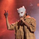 Ein Mann mit einer weißen Maske steht auf der Bühne und singt. (Foto: IMAGO / Christian Grube)