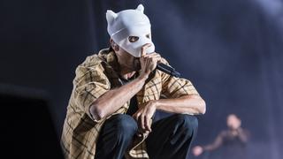 Ein Mann mit einer weißen Maske steht auf der Bühne und singt. (Foto: IMAGO / Christian Grube)