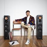 Eren sitzt zwischen zwei Lautsprecherboxen vor einer weißen Wand. (Foto: Eren Selcuk)