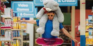 Channing Tatum, aka Jeff im Film,  läuft durch den Gang eines Geschäfts. Er trägt eine gelbe Sonnenbrille, einen pinken Schwimmreif um seine Hüften und auf seinen Schultern sitzt ein riesiger Teddybär. (Foto: leoninedistribution)