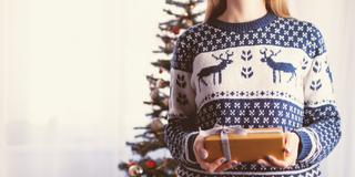 Eine Frau überreicht vor einem Weihnachtsbaum ein Geschenk (Foto: pixabay.com/JESHOOTS-com)