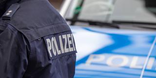 Schriftzug Polizei auf der Rückseite einer Jacke eines Polizisten vor einem Streifenwagen  (Foto: IMAGO / Deutzmann)