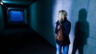 Eine Frau schaut sich auf ihrem Heimweg in einer dunklen Unterfühung ängstlich um. (Foto: IMAGO / Shotshop)