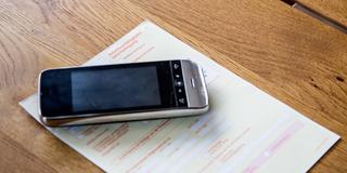 Ein Telefon liegt auf einer Arbeitsunfähigkeitsbescheinigung (Foto: IMAGO / Fotostand)