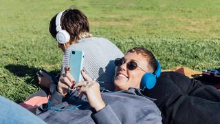 Zwei Frauen liegen auf einer Wiese und hören über Kopfhörer etwas auf ihrem Smartphone. (Foto: IMAGO / Westend 61)