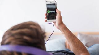 ein Junge liegt im Bett und schaut auf sein Handy. Dort ist Spotify geöffnet. (Foto: IMAGO / YAY Images)