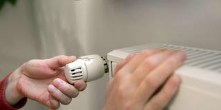 Jemand fasst an einen Heizkörper und den Thermostatregler (Foto: IMAGO / Shotshop)