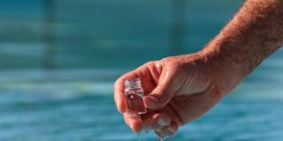 Jemand entnimmt in einem Freibad eine Wasserprobe (Foto: IMAGO / HMB-Media)