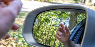 Eine Zigarette wird auf einem Waldparkplatz aus einem Auto gehalten (Foto: IMAGO / Pressedienst Nord)