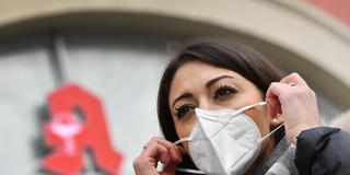 Eine Frau mit Mundschutzmaske steht vor einer Apotheke. (Foto: IMAGO / Sven Simon)