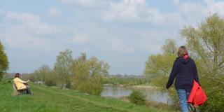 Eine Spaziergängerin auf einem Deich neben einem Fluss.  (Foto: IMAGO / Eckhard Stengel)