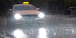 Kräftige Regenfälle. Ein Taxi fährt bei Starkregen durch eine regennasse Straße. (Foto: IMAGO / Gottfried Czepluch)