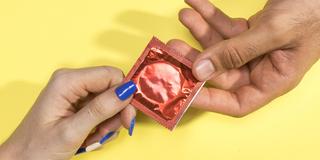 Zwei Hände übergeben sich eine Kondompackung. (Foto: IMAGO / YAY Images)