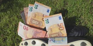 Symbolbild. Fussballschuh mit Euros auf einem Rasen. (Foto: IMAGO / blickwinkel /Steidi)