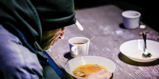 Ein Obdachloser sitzt in einer Kältehilfe-Einrichtung beim Essen (Foto: IMAGO / Funke Foto Services)