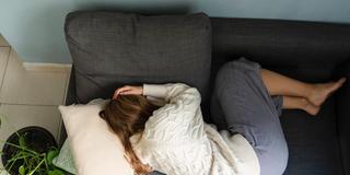 Junge Frau liegt gekrümmt auf dem Sofa (Foto: IMAGO / Westend61)