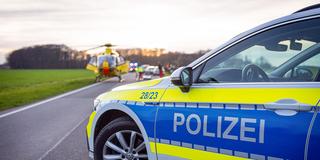 Ein Einsatzfahrzeug der Polizei bei einem Verkehrsunfall auf einer Landstraße. Rettungsdienst und Hubschrauber im Hintergrund (Foto: IMAGO / Fotostand)
