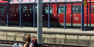 Eine Rucksacktouristin sitzt auf dem Boden und wartet auf den Zug. (Foto: IMAGO / Action Pictures)