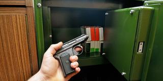 Jemand hält eine kleine Handfeuerwaffe vor einem Tresor für die sichere Aufbewahrung (Foto: IMAGO / Niehoff)