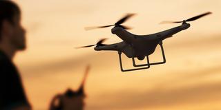 Eine Person steuert eine fliegende Drohne im Sonnenuntergang. (Foto: IMAGO / Dreamstime)