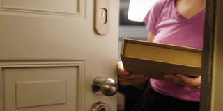 Eine Frau hält ein Paket hinter der Haustür in der Hand (Foto: IMAGO / photothek)