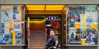 Ein Rollstuhlfahrer steht vor dem Treppenaufgang eines Kinos (Foto: IMAGO / Funke Foto Services)