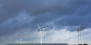 Stromleitungen laufen über einer Solaranlage vor einem Windrad (Foto: IMAGO / Westend61)