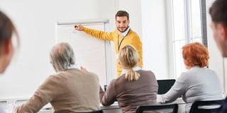 Dozent in einem Kurs einer VHS bei einem Vortrag (Foto: IMAGO / Zoonar II /  Robert Kneschke)