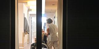 Pflegekraft schiebt eine Person im Rollstuhl (Foto: IMAGO / Sven Simon)