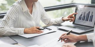 Zwei Personen am Schreibtisch besprechen Firmencharts (Foto: IMAGO / Zoonar / Chalirmpoj Pimpisarn)