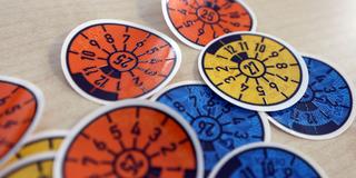 Tüv-Plaketten verschiedener Gültigkeit liegen auf einem Tisch (Foto: IMAGO / Rene Traut)