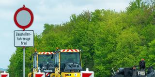 Auf einer deutschen Autobahn wird die Fahrbahn erneuert. Baustellenfahrzeuge wie Walzen und Asphaltmaschinen stehen am Fahrbahnrand. (Foto: IMAGO / Bihlmayerfotografie)