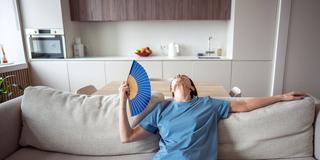 Eine Frau mittleren Alters wedelt sich Luft mit einem Fächer zu (Foto: IMAGO / Zoonar)