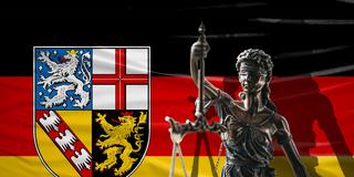 Die Justitia-Figur mit Waage vor der Saarland-Flagge steht für Rechtsstaatlichkeit und Gerichtsbarkeit (Foto: IMAGO / Bihlmayerfotografie)