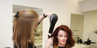 Eine Friseurauszubildende übt an einer Puppe (Foto: IMAGO / epd / Steffen Schellhorn)