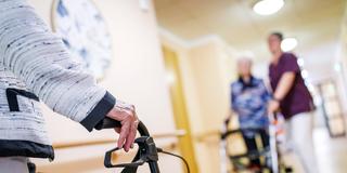 Senioren mit Rollator und eine Pflegekraft sind auf einem Gang  (Foto: IMAGO / Andreas Franke)