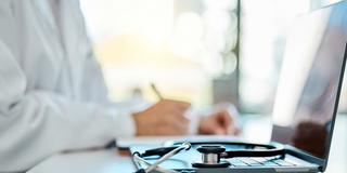 Ein Stethoskop liegt auf dem Computer eines Arztes im Hintergrund (Foto: IMAGO / YAY Images)