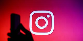 Weißes Instagram-Logo vor rot-violettem Hintergrund. Schatten einer Hand, die ein Smartphone hält. (Foto: IMAGO / NurPhoto)