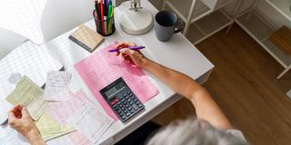 Eine Frau sitzt am Schreibtisch mit Unterlagen und Rechner (Foto: IMAGO / Westend61)