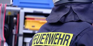 Symbolbild Feuerwehr. Ein Feuerwehrmann steht vor dem Einsatzwagen. (Foto: IMAGO / Martin Wagner)