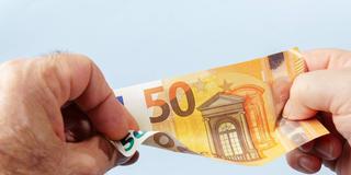 Zwei Hände ziehen agegensätzlich an einem 50-Euro-Schein (Foto: IMAGO / Zoonar)