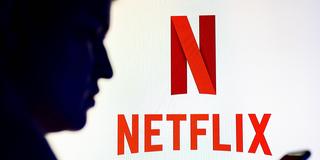 Mann am Handy vor dem roten Netflix-Logo (Foto: IMAGO / SOPA Images)