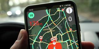 Jemand hält im Auto ein Smartphone in der Hand, auf dem eine Blitzer-Warn-App geöffnet ist (Foto: IMAGO / Hanno Bode)
