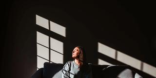 Eine Frau sitzt im Sonnenlicht eines großen Fensters aufeiner Couch (Foto: IMAGO / Cavan Images)