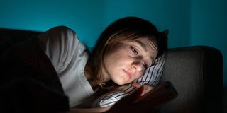 Eine Frau liegt im dunkeln und blickt entsetzt auf ihr Smartphone (Foto: IMAGO / Zoonar)